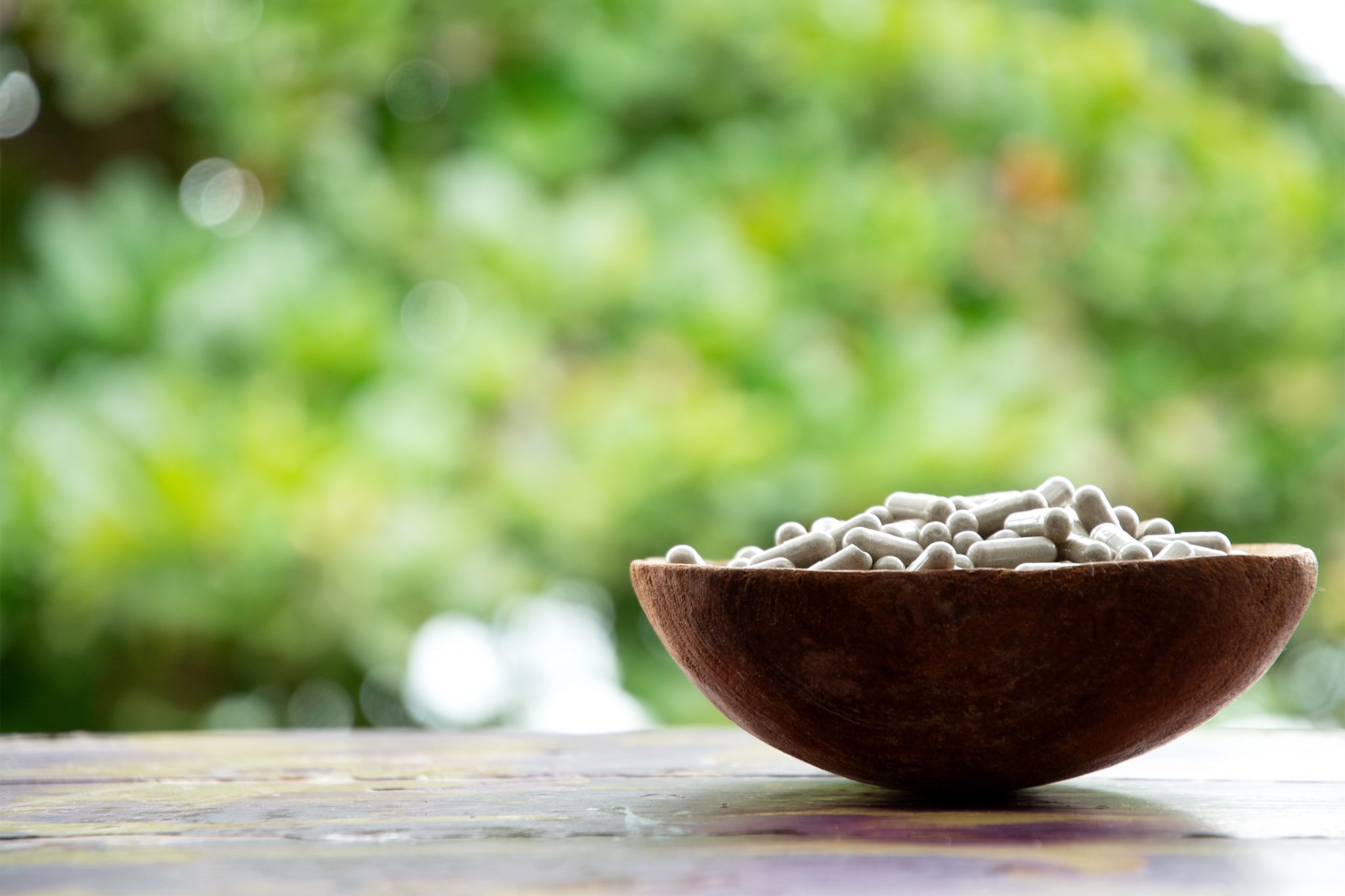 A wooden bowl filled with capsules of psilocybin mushroom powder, placed on a table.