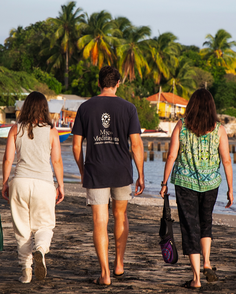 Guests walking along beach while integrating psilocybin insights.