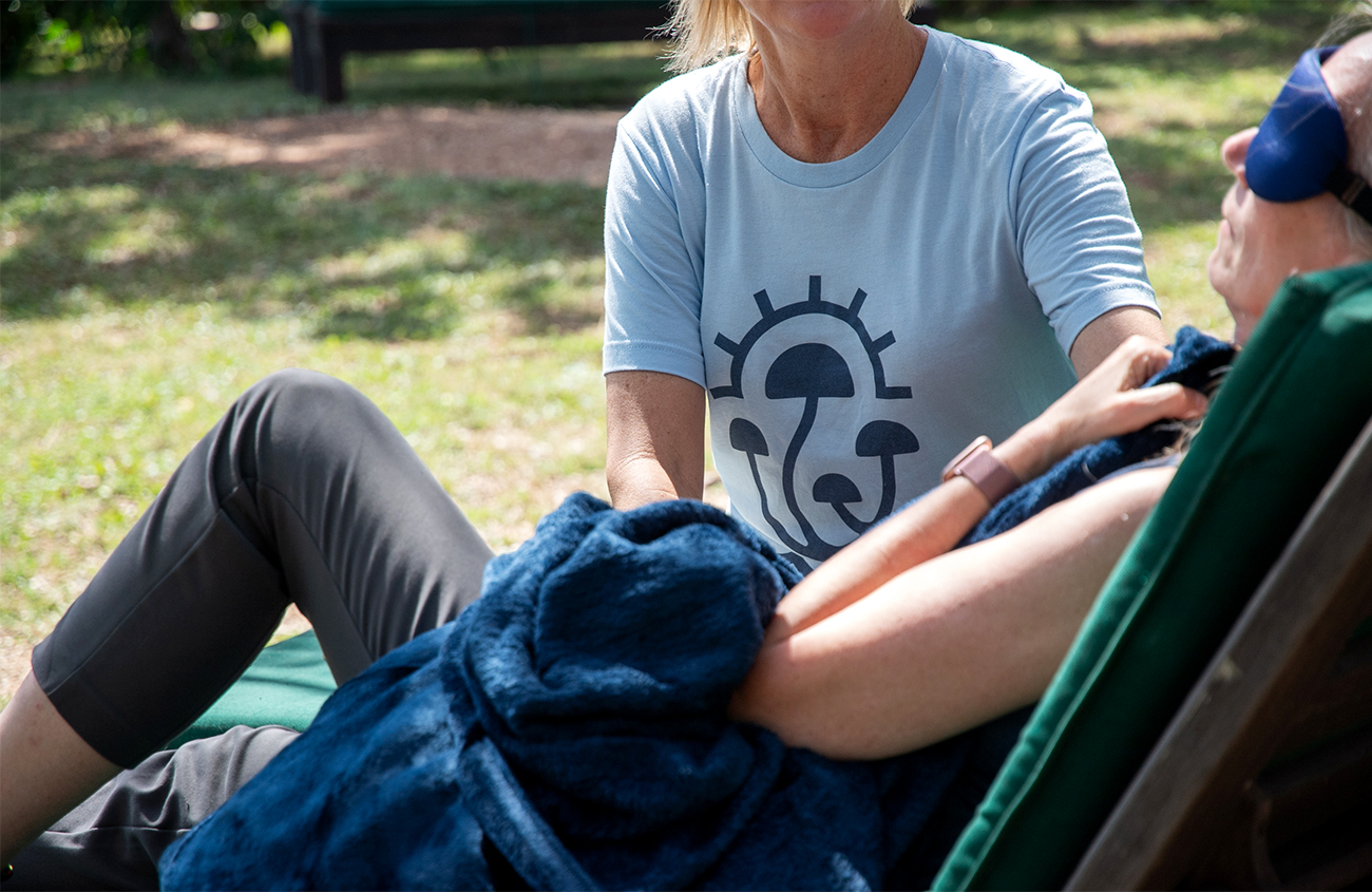 A woman wears eye shades and a blanket while a therapist sits beside her.