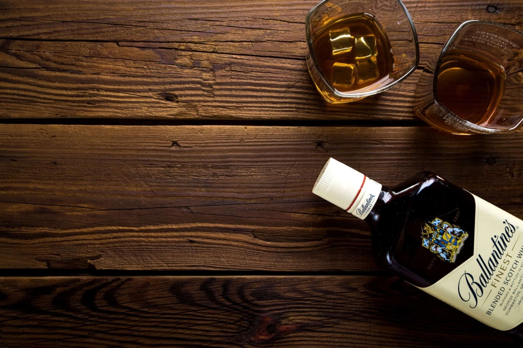 Scotch bottle and two tumbler glasses with scotch on a wooden desk.