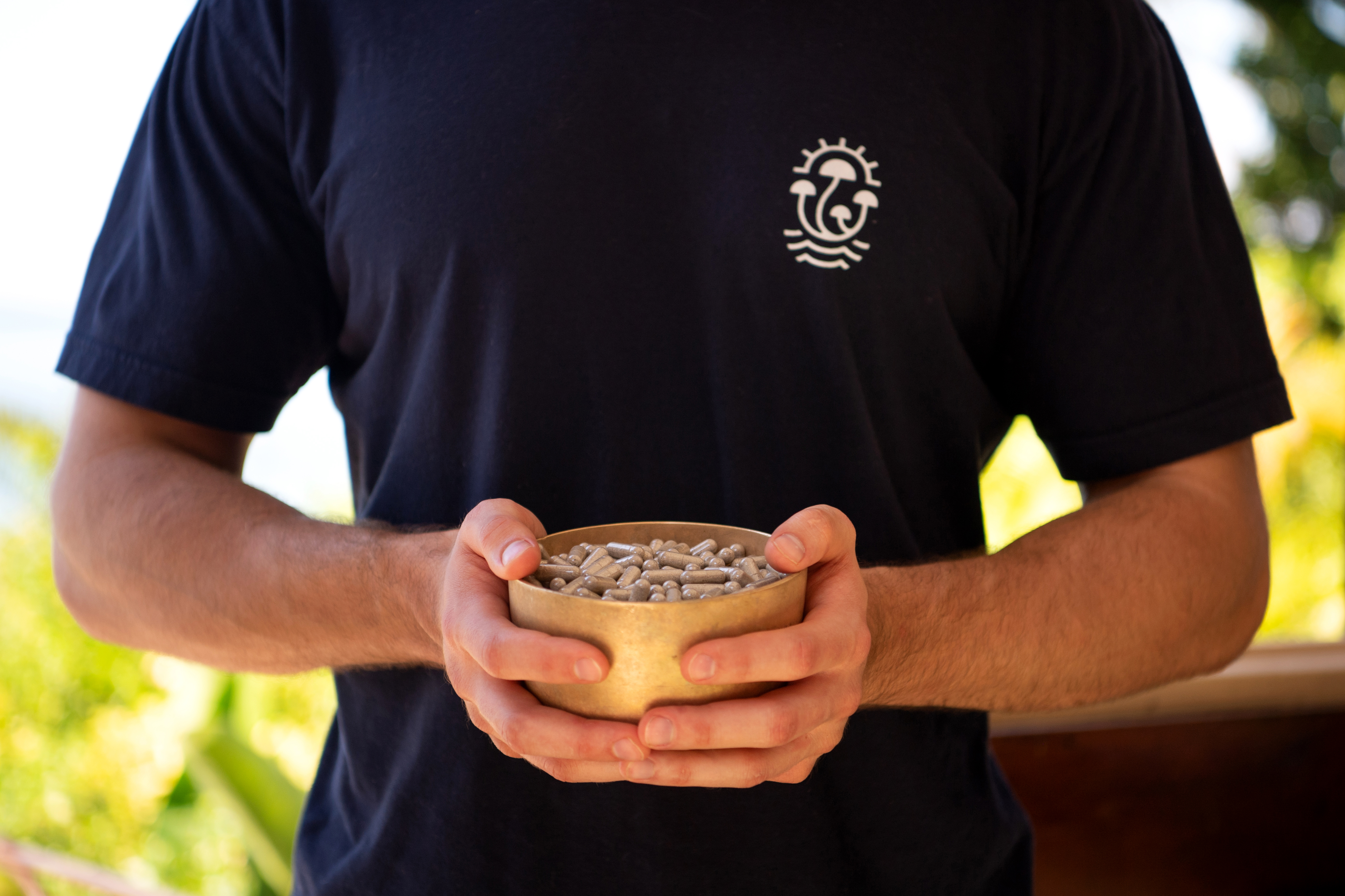 Man wearing a MycoMeditations t-shirt holding a bowl of psilocybin mushroom capsules.