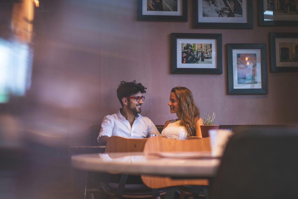 A couple sitting in a booth smiling at one another.