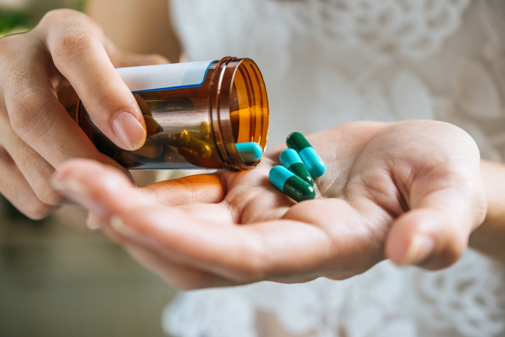 A woman empties a bottle of bipolar medication pills into her hand.