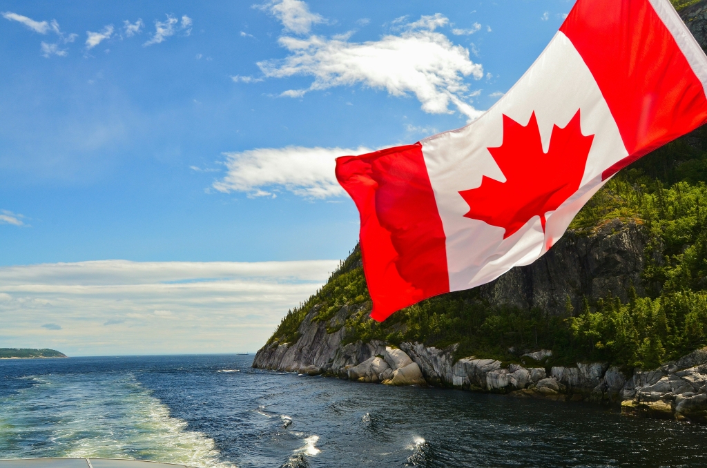 A Canadian flag with scenic view of waves and a mountain overlooking the water in the background