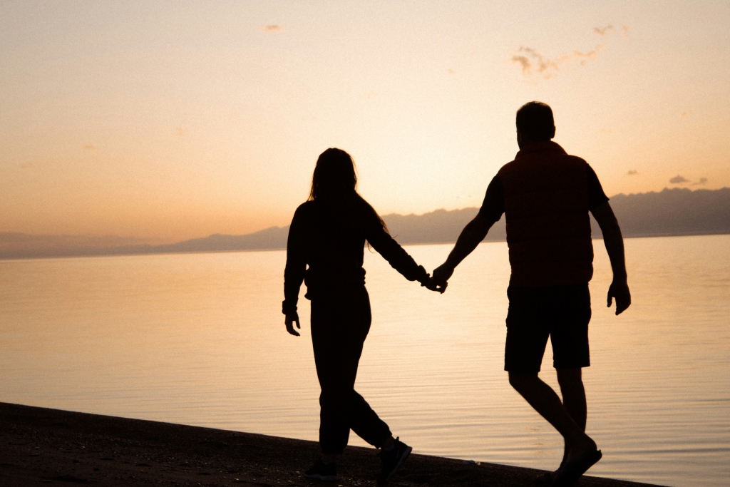 Silhouette of a couple walking along the shore of a lake together with a sunset background.